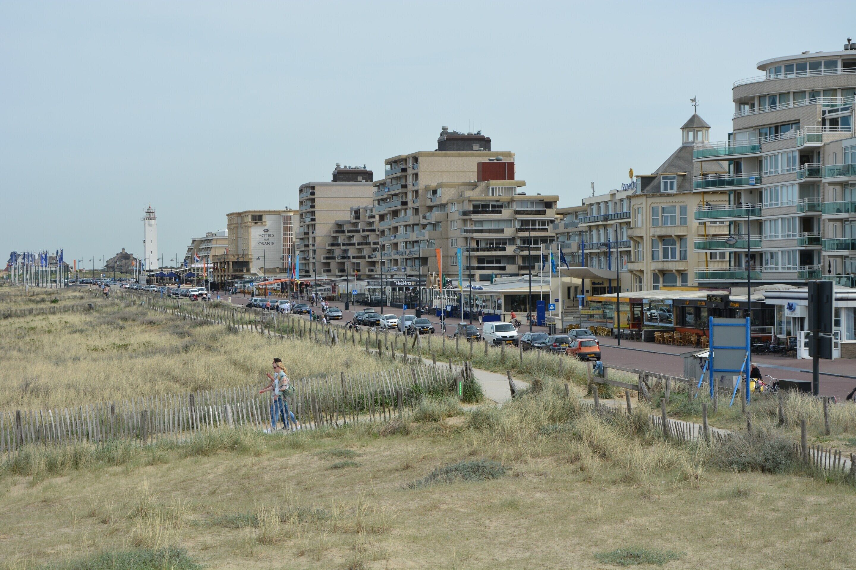 Un hôtel situé sur la côte, avec plusieurs étages, une vue sur la plage et une promenade bordée de voitures garées.