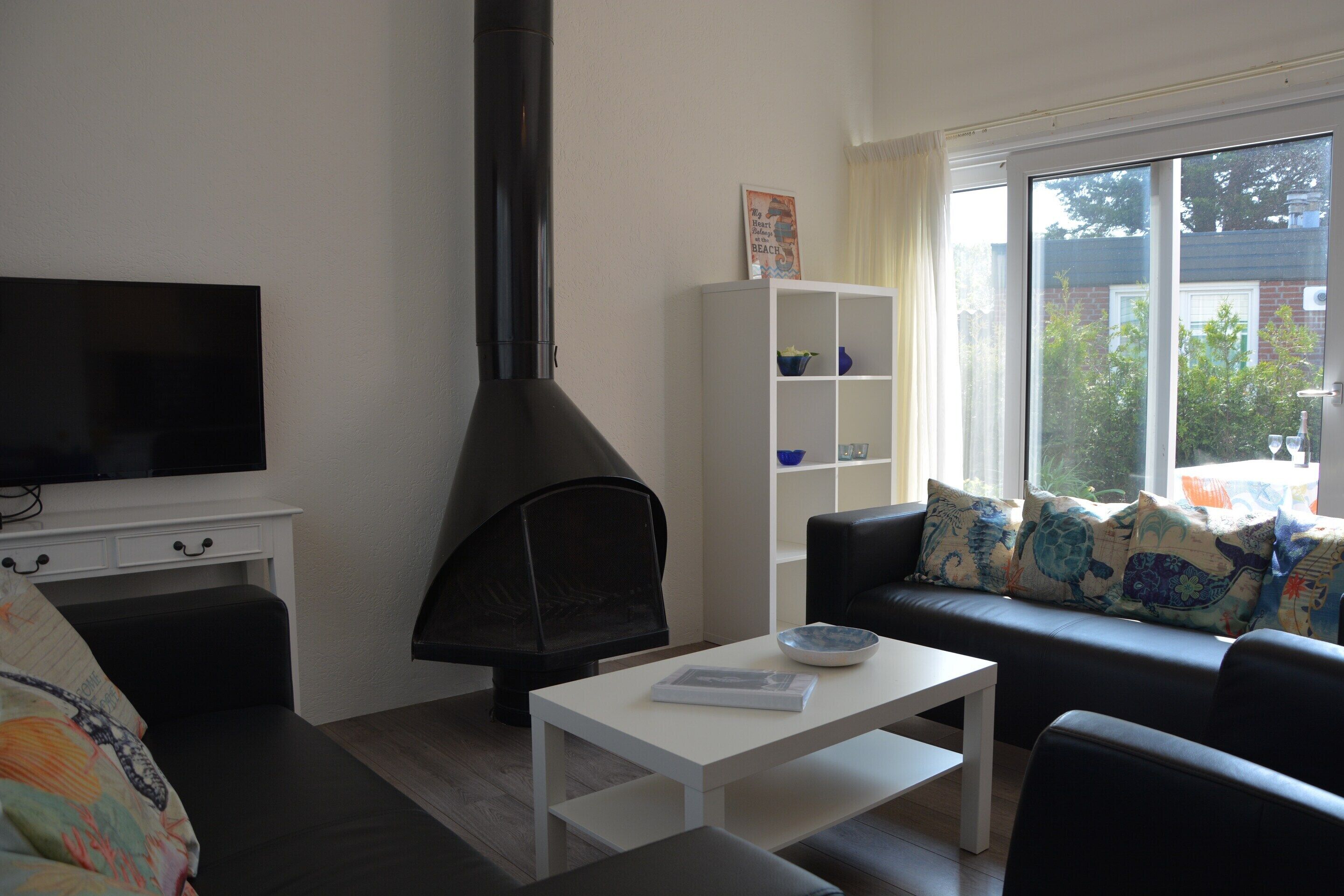 A living room with a fireplace, a sofa with decorative pillows, a television, and a window with a view of the outside.