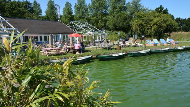 Een restaurant aan het meer met terras, boten en een overdekt gedeelte.