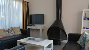 Een woonkamer met een zwarte bank, een witte salontafel, een flatscreen-tv en een zwarte open haard.