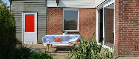 A house with a red door, a covered patio with a table, and a brick exterior.