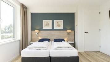 A double bed with two bedside tables, a window with curtains, and a door.