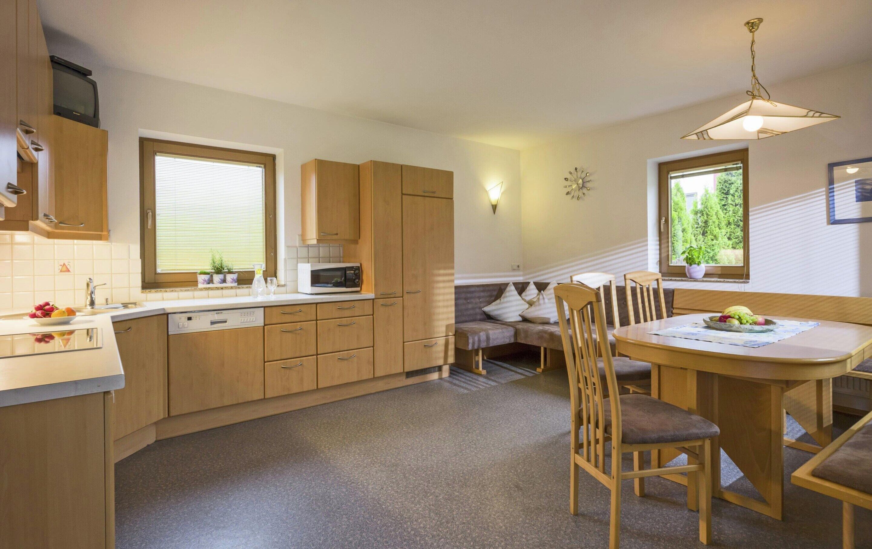 A compact kitchen with wooden cabinets, a microwave, a sink, and a dining area with a table and chairs.