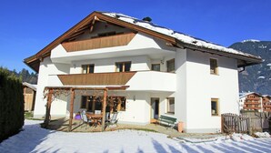 A two-story building with a covered patio area, a bench, and a snow-covered roof. - Residence in Kaltenbach Near ski Lifts (Kaltenbach)