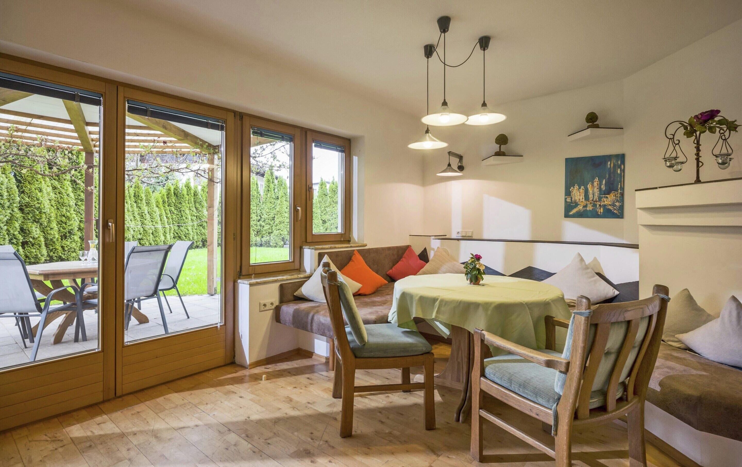 Un coin repas accueillant avec une table ronde, des chaises en bois et un banc. De grandes fenêtres offrent une vue sur un jardin.