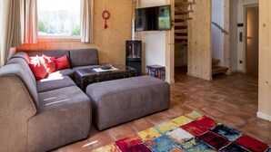 A cozy living room with a sectional sofa, a flat-screen TV, a fireplace, and a staircase leading to another level. - Awe-inspiring Chalet Near Ski Area in Sankt Georgen ob Murau (Sankt Georgen am Kreischberg)