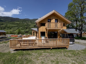 A two-story wooden cabin with a balcony, a hot tub, and a gravel driveway. - Awe-inspiring Chalet Near Ski Area in Sankt Georgen ob Murau (Sankt Georgen am Kreischberg)