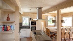 A modern kitchen with white cabinets, a central island, and a dining area with wooden chairs and a table. - Awe-inspiring Chalet Near Ski Area in Sankt Georgen ob Murau (Sankt Georgen am Kreischberg)