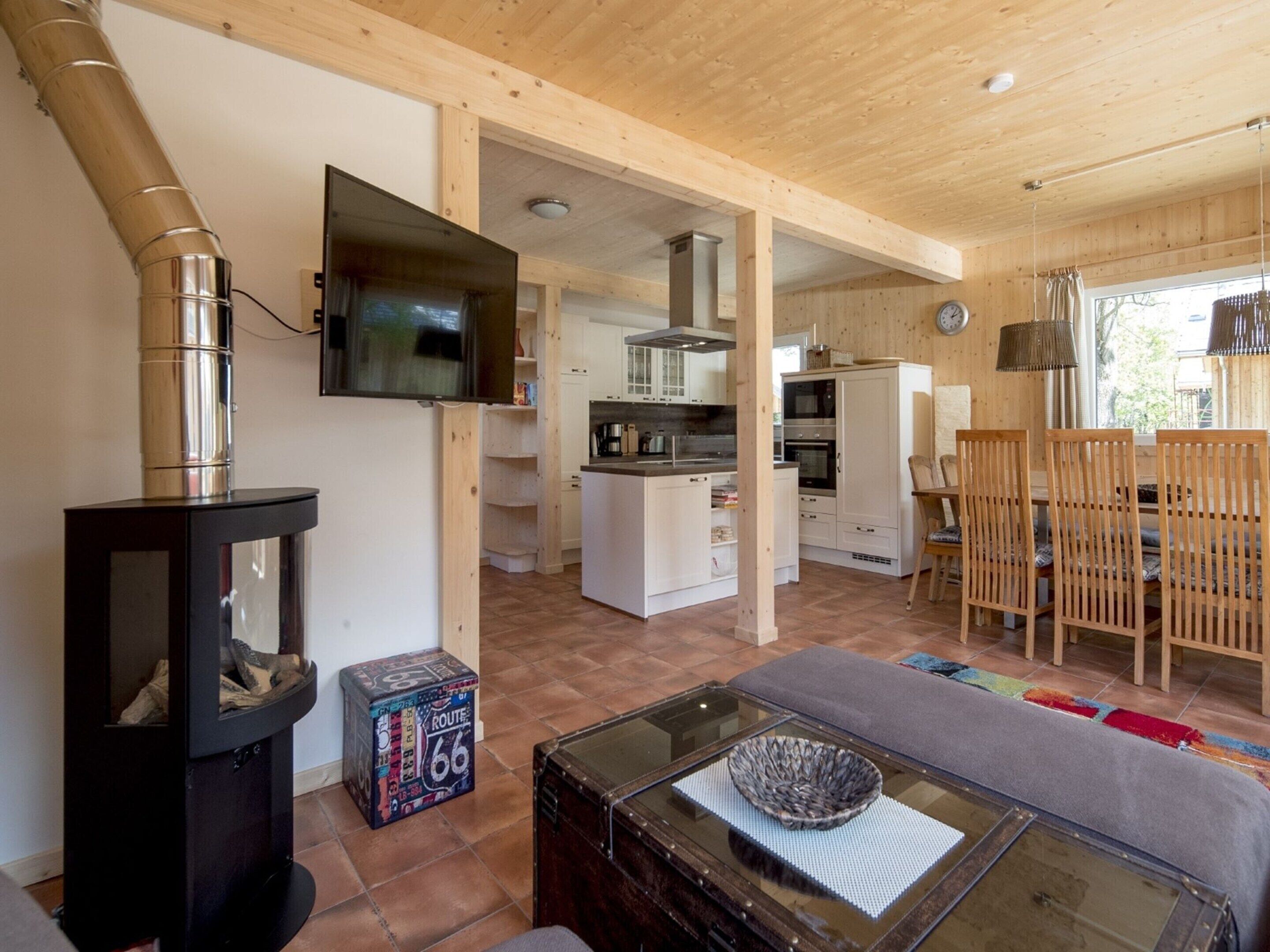 A modern kitchen with white cabinets, a large TV, and a dining area with wooden chairs and a glass table.