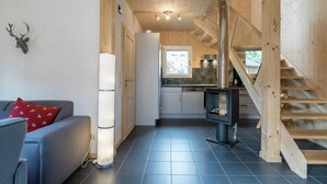 Una cucina moderna con piano cottura integrato, una zona pranzo con un divano grigio e un cuscino rosso, e una scala che conduce a un livello superiore.