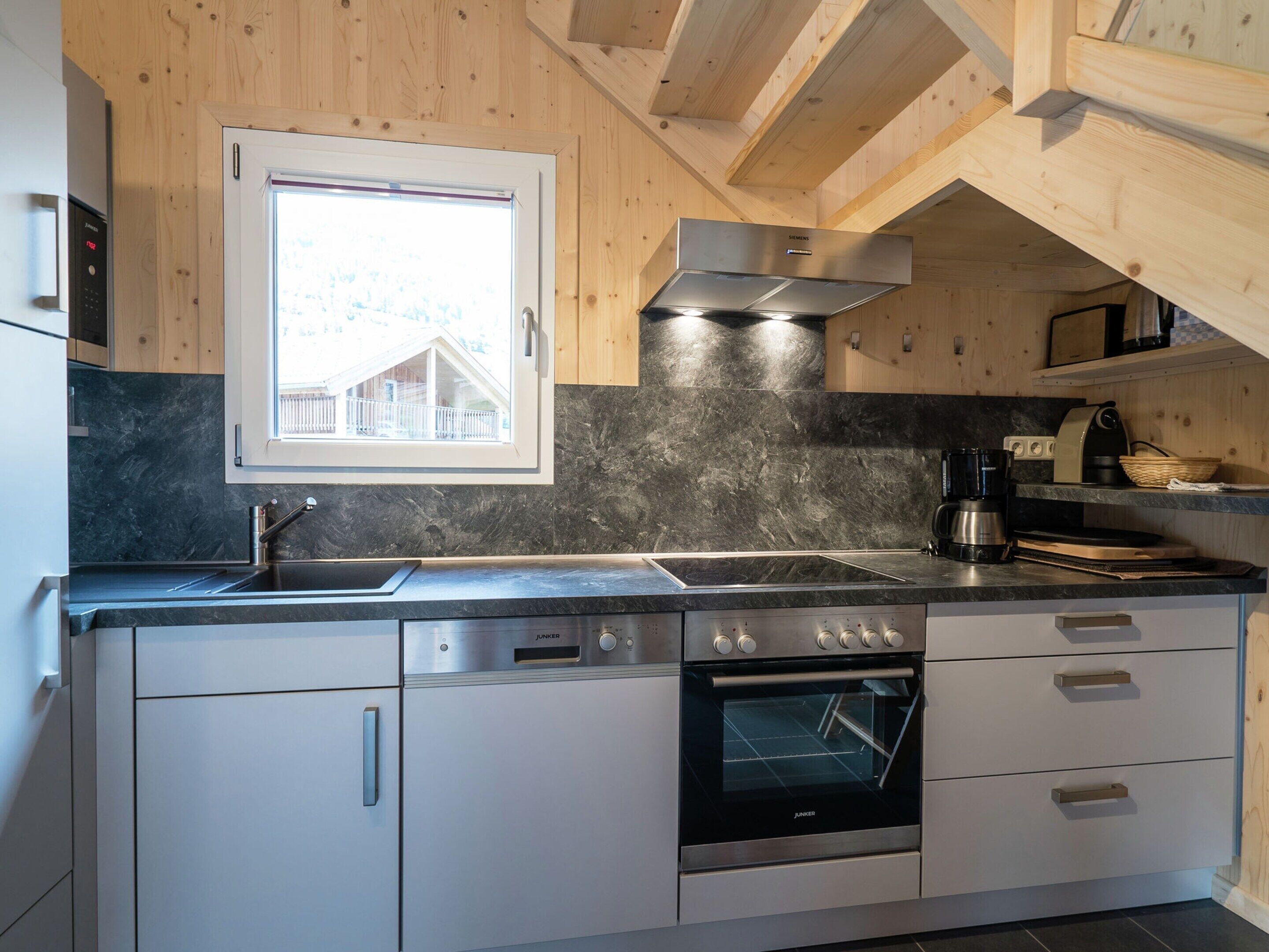 Eine moderne Küche mit eingebautem Backofen, einem Edelstahlkochfeld und einem Fenster mit Blick auf ein Haus.