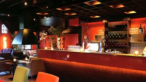 Zona de bar con asientos, una barra con un ordenador y estantes con botellas y vasos.