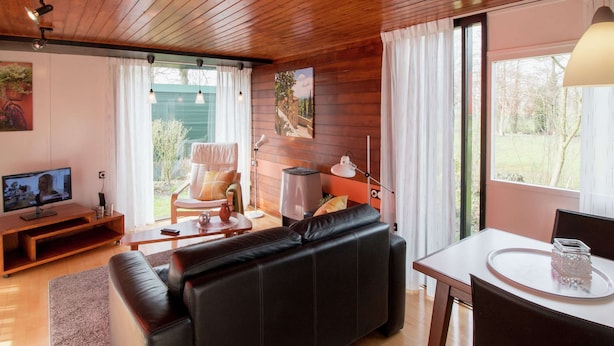 Una sala de estar acogedora con un sofá de cuero negro, piso de madera, televisor y un comedor con mesa y sillas.