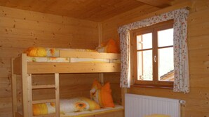 A wooden cabin bedroom with bunk beds, a window with floral curtains, and a radiator.