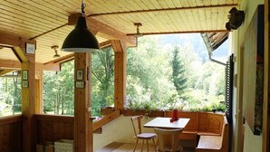 Uma cabana de madeira com área de refeições, um banco e vista para a floresta.