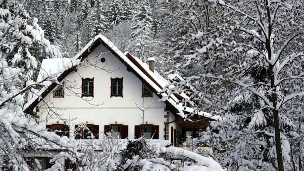 Uma casa coberta de neve com telhado íngreme, rodeada por árvores.