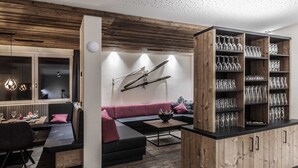 A modern living room with a wooden accent wall, a black sofa, a wooden cabinet with glassware, and a dining area with a table and chairs. - Chalet in Gaschurn Near Ski Lift (Gaschurn)