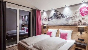 A modern hotel room with a large bed, a sliding glass door leading to a balcony, and a wall-mounted artwork depicting a snowy mountain scene. - Chalet in Gaschurn Near Ski Lift (Gaschurn)