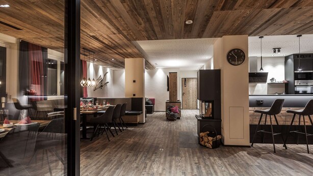 A modern interior with a wooden ceiling, a dining area with a table and chairs, a kitchen with a stove and bar seating. - Chalet in Gaschurn Near Ski Lift (Gaschurn)