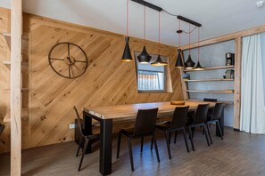 Un espace repas agrémenté d’un mur en bois disposé en motif chevron, d’une horloge murale ronde, d’une table à manger en bois avec six chaises et de luminaires suspendus.