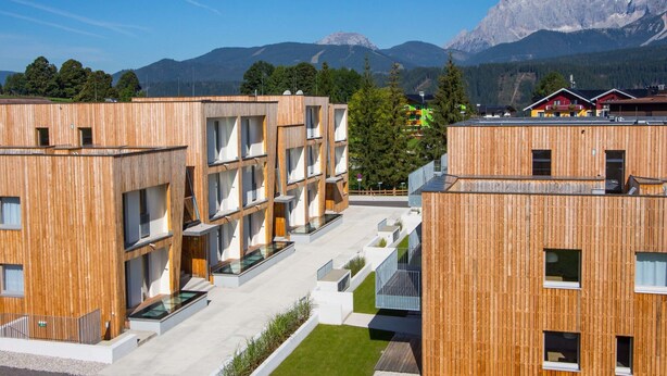 A modern wooden building with multiple floors and balconies, surrounded by a well-maintained lawn and a mountain backdrop. - Apartment With Sauna (Schladming)