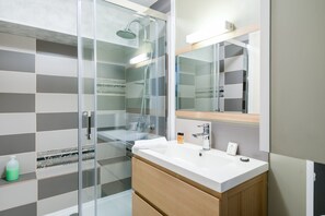 A modern bathroom with a glass shower enclosure, a white sink, and a mirror above it. - Apartment in Port-en-bessin Near Seashore (Port-en-Bessin-Huppain)