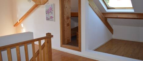 A loft bedroom with a skylight, wooden beams, and a white wall with a floral painting.