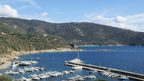 Un port de plaisance avec des bateaux amarrés, un phare et un paysage vallonné en arrière-plan.