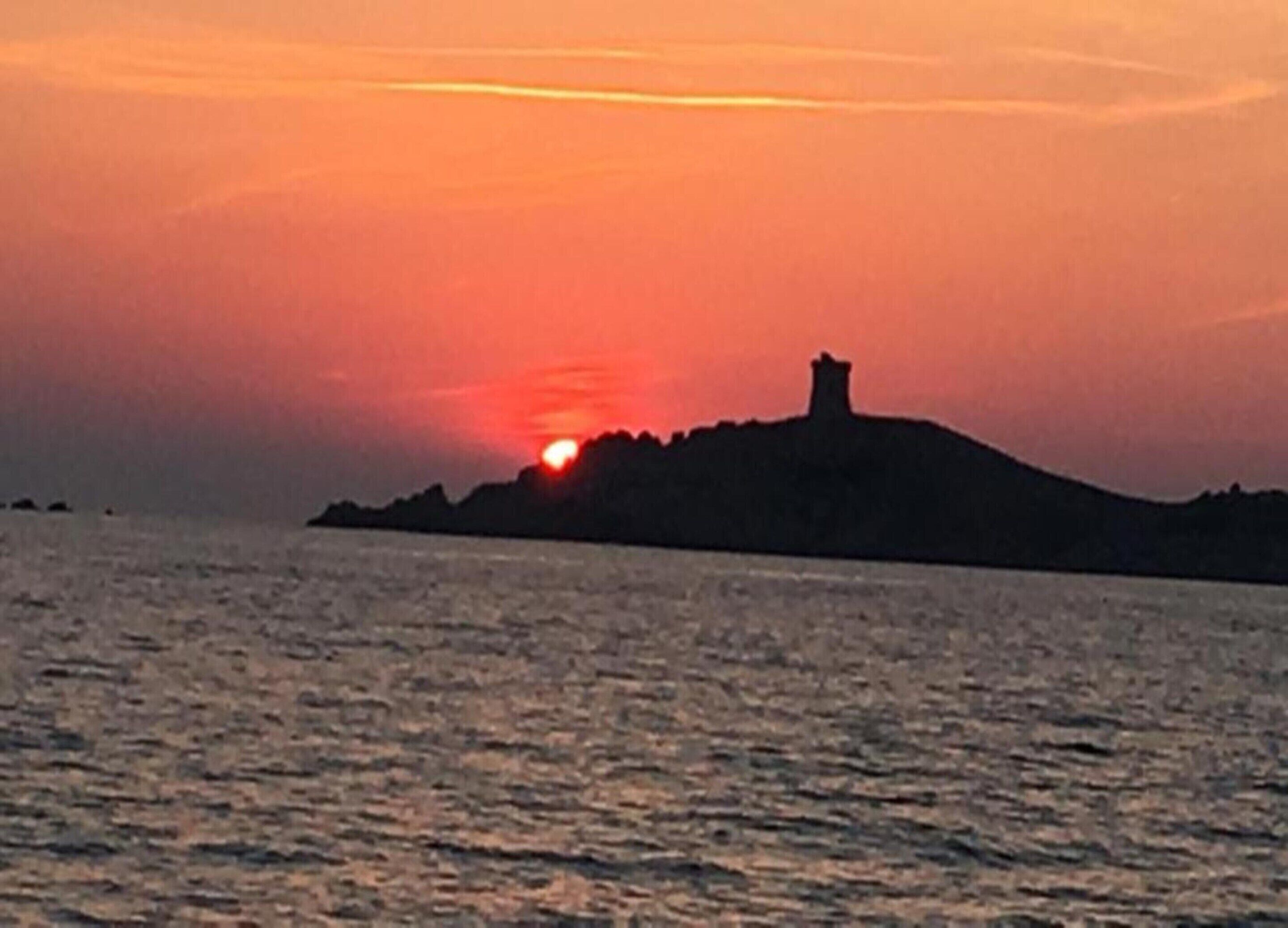 A sunset over a body of water with a silhouette of a hill and a tower.