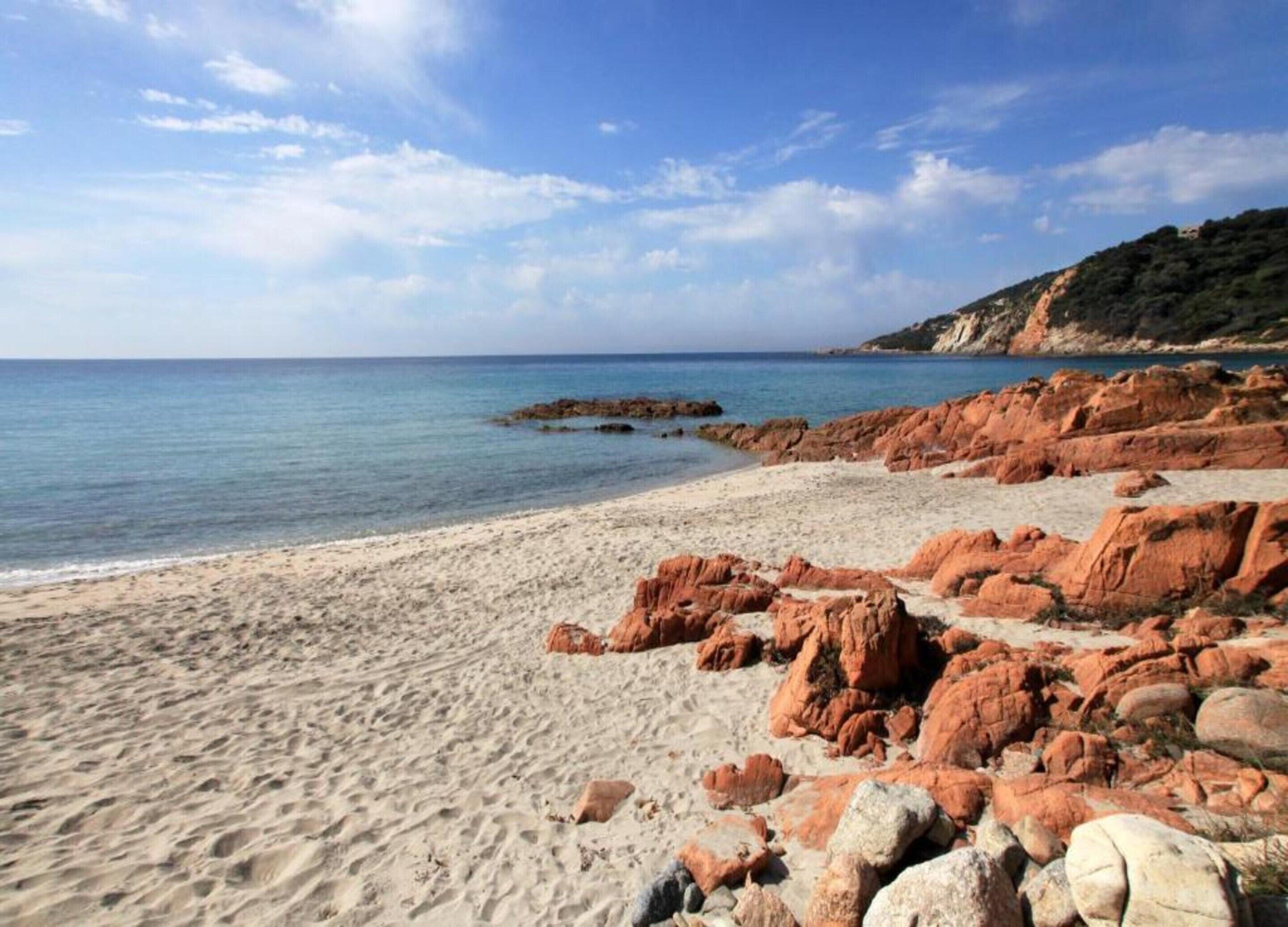 A beach with red rocks and a clear sky.
