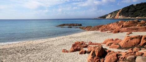 A beach with red rocks and a clear sky.