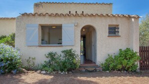 Un bâtiment rustique avec un toit en tuiles, une porte d’entrée centrale et deux fenêtres dotées de volets.