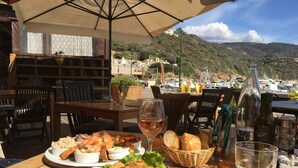 Une table dressée avec des fruits de mer, du pain et des boissons, offrant une vue sur une marina et des collines.