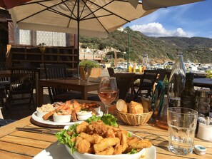 Une table dressée avec des fruits de mer, du pain et des boissons, offrant une vue sur une marina et des collines.