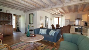 A spacious living room with a blue sofa, a wooden dining table, and a kitchen area with cabinets and appliances. - Cozy Cottage in Roussines, Dordogne (Roussines)