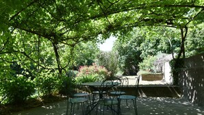 An outdoor patio area with a table and chairs under a tree canopy. - Holiday Home in Ardeche Near Chateau Ventadour (Lalevade-d'Ardeche)
