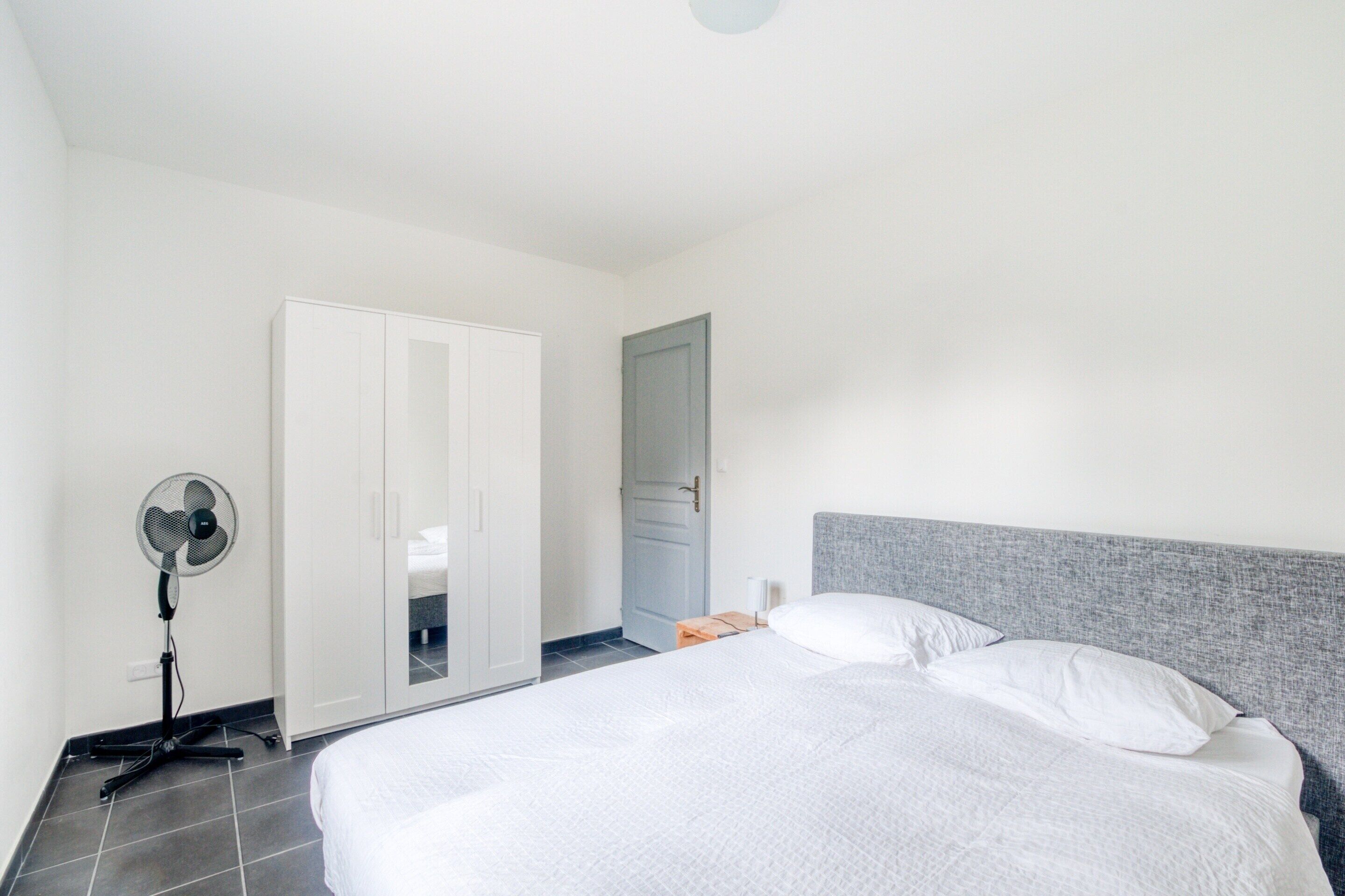 Un dormitorio con cama, ventilador, armario y puerta.