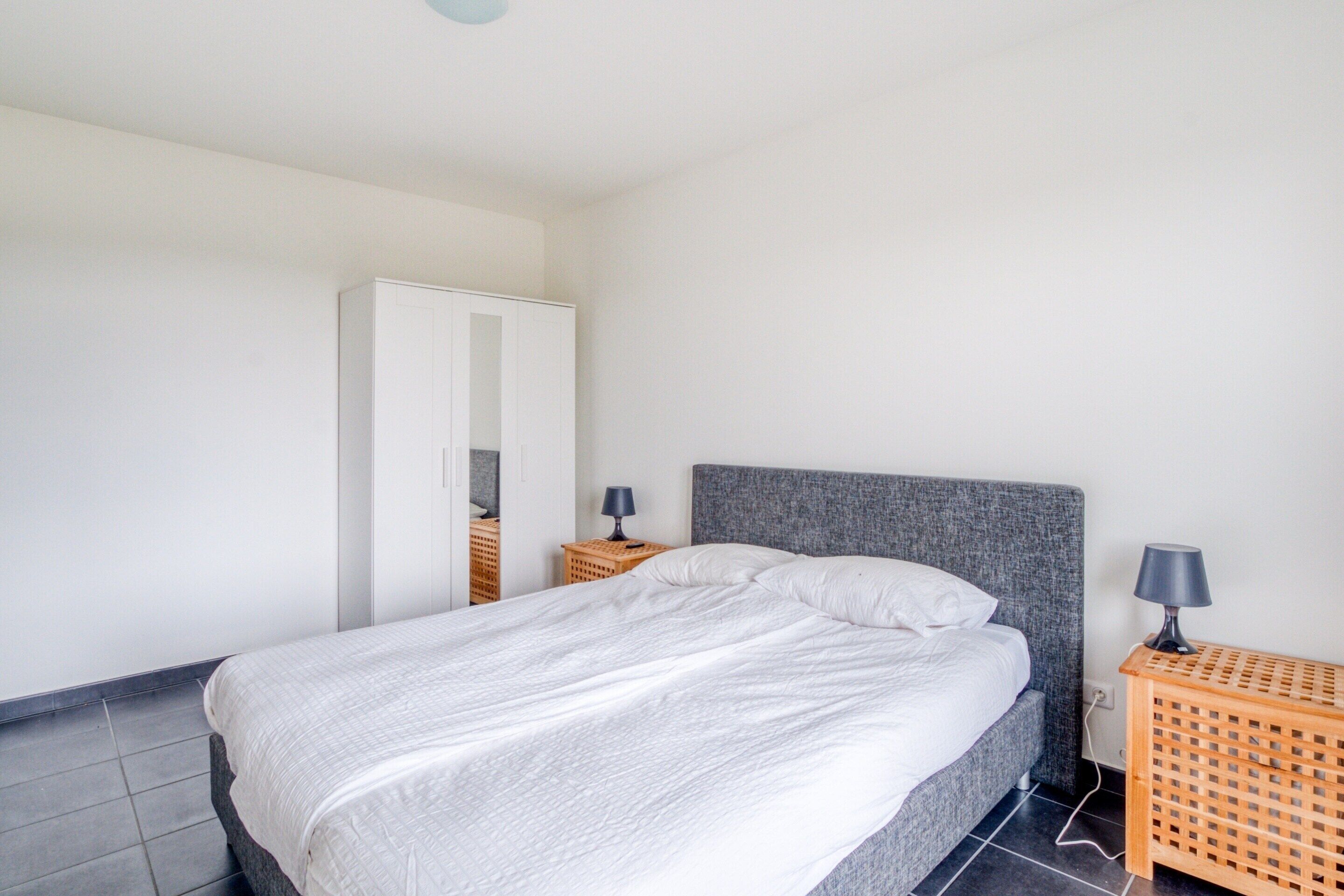 Un dormitorio con cama, armario, dos mesitas de noche con lámparas y suelo de baldosas.