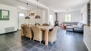 Un salón amplio con mesa de comedor, sillas de mimbre, un sofá gris y chimenea.