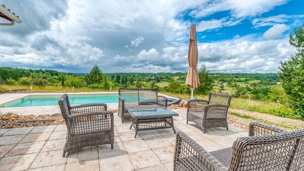 Un patio al aire libre con mobiliario de mimbre, piscina y vistas al campo.