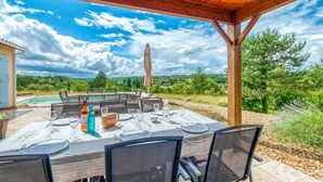 Un área de comedor al aire libre con una mesa preparada para cuatro, con vista a una piscina y un paisaje pintoresco.