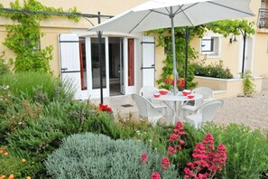 An outdoor seating area with white chairs and a table, surrounded by various plants and flowers. - Modern Terrace Stay Montbrun (Montbrun-les-Bains)