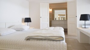 Une chambre à coucher comprenant un lit, deux tables de chevet, un miroir et une porte ouverte donnant sur une salle de bain.