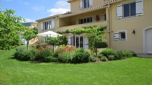 Un bâtiment à deux étages doté d’un balcon, d’un jardin avec différentes espèces de plantes et d’une porte blanche.