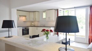 Une cuisine moderne avec des meubles blancs, un coin repas comprenant une table, des chaises et une lampe.