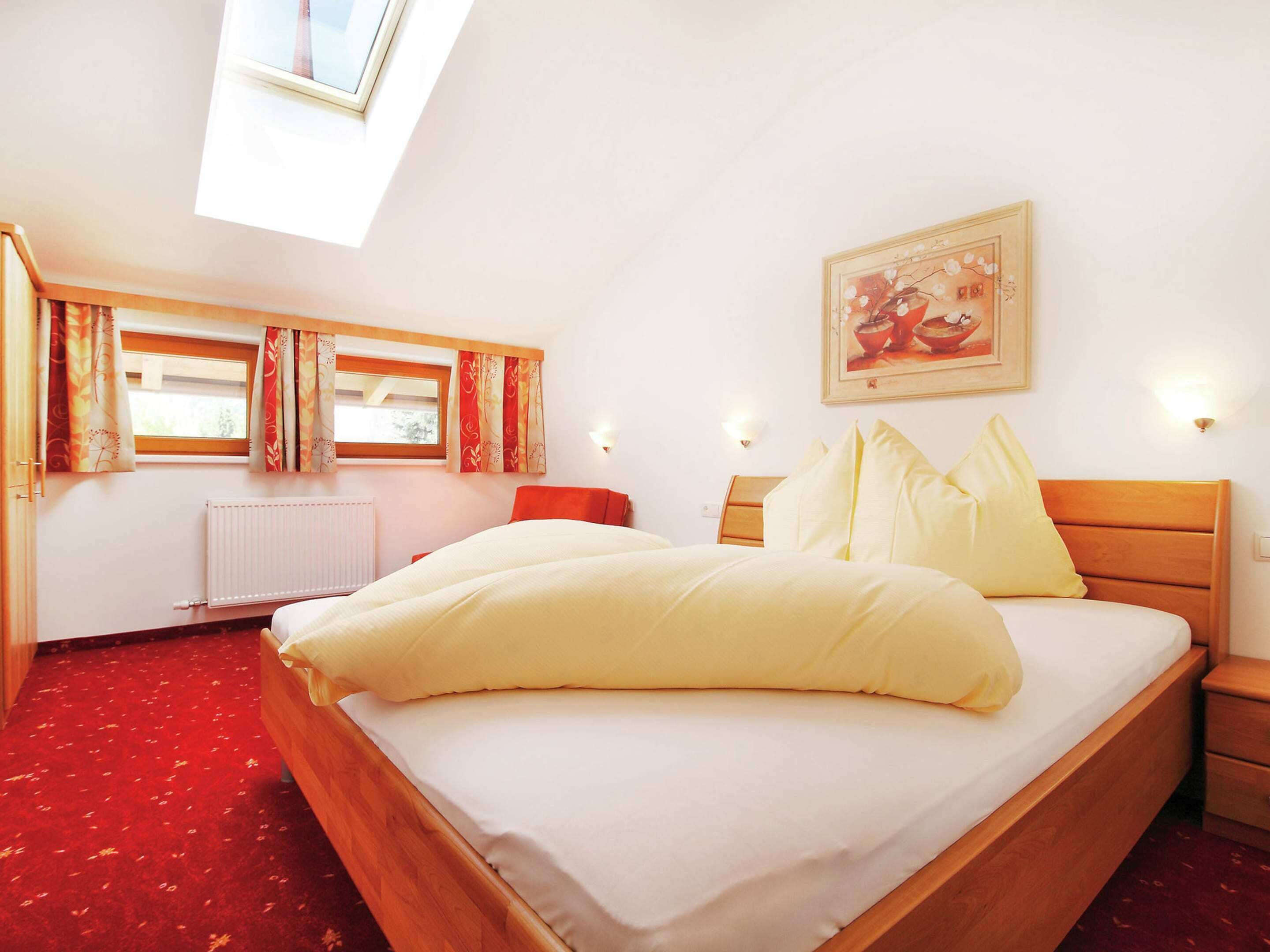 Un dormitorio con cama, ventana con cortinas, radiador, mesita de noche y lámpara fijada a la pared.
