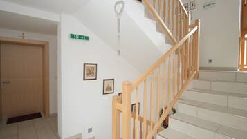 Una escalera con barandillas y pasamanos de madera que conduce a un piso superior. Hay cuadros enmarcados en las paredes y una señal de salida verde.