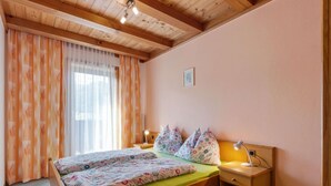 A bedroom with a wooden ceiling, a bed with floral bedding, a nightstand with a lamp, and a window with sheer curtains. - Spacious Apartment in Mittersill near Ski Area (Mittersill)