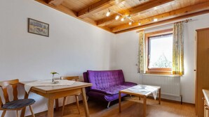A cozy room with a wooden ceiling, a purple sofa, a wooden dining table with chairs, and a window with curtains. - Spacious Apartment in Mittersill near Ski Area (Mittersill)