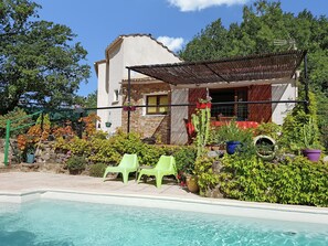 Ein Poolbereich mit einem Haus, grünen Stühlen und Topfpflanzen.